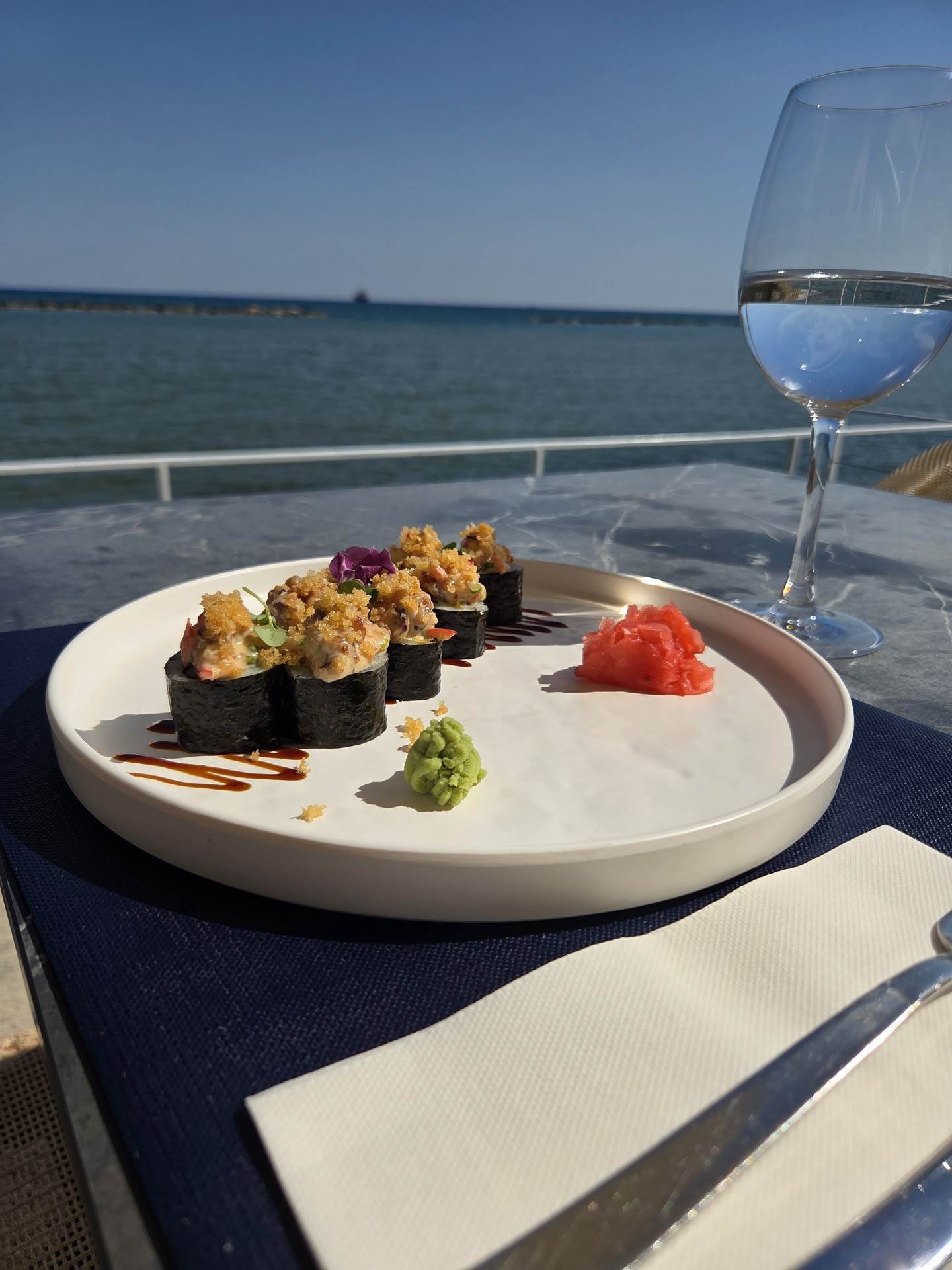 A sushi plate and a glass of white wine with the sea behind
