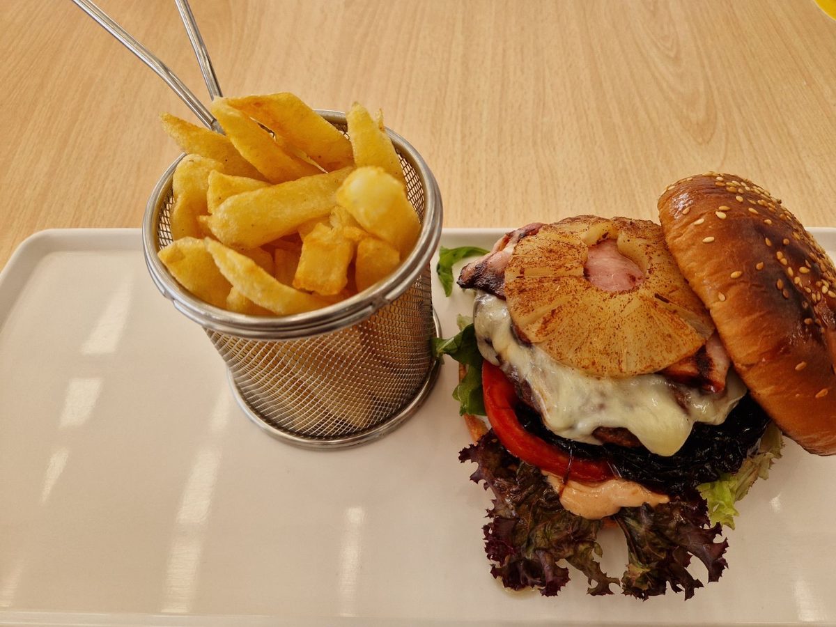 A grilled burger with pineapple and a basket of chips